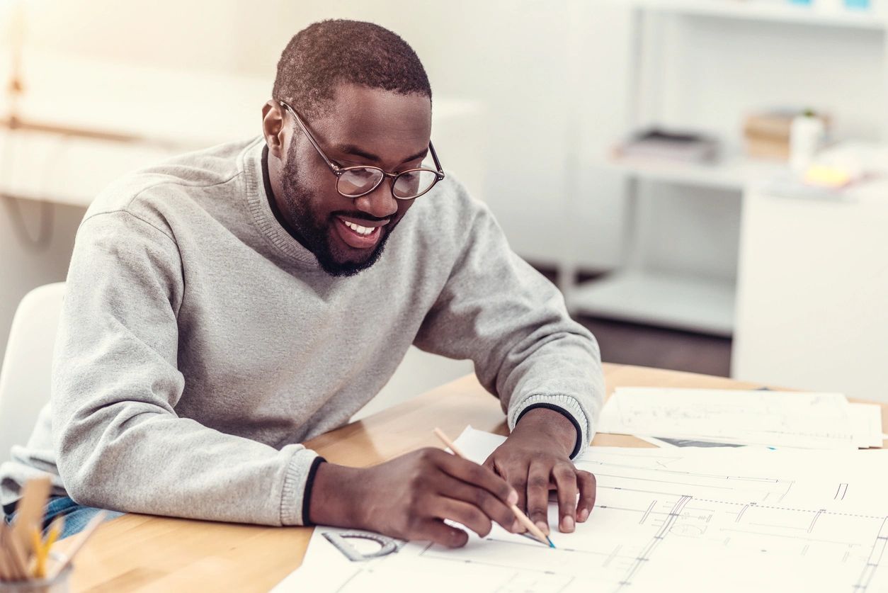 African American male with glasses wearing a grey sweater smiling while writing